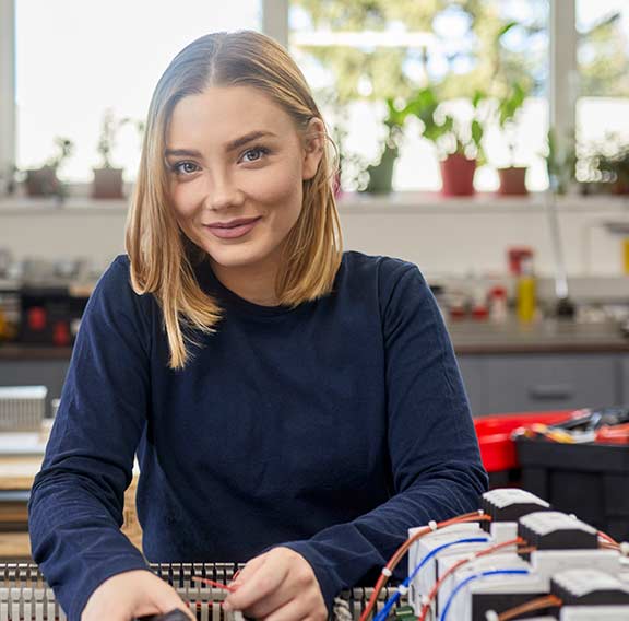 Portrait of smiling female electrician working on circuitry in workshop