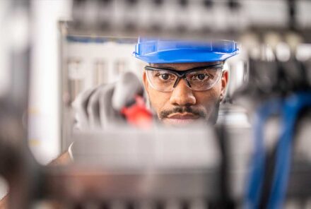 Young apprentice wearing safety glasses while connecting wires in distribution board